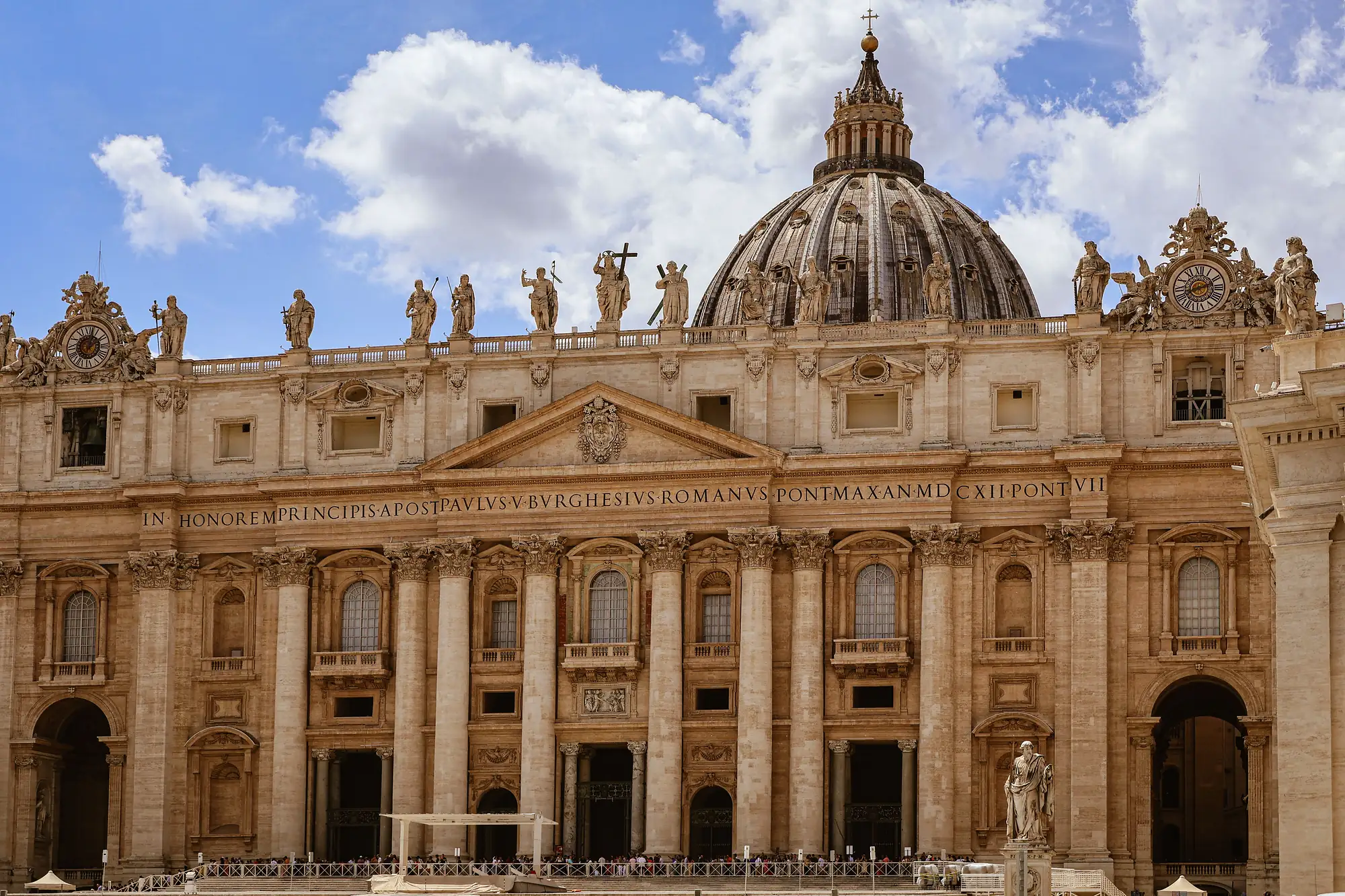 The facade and dome of St. Peter's Basilica beneath a blue sky.