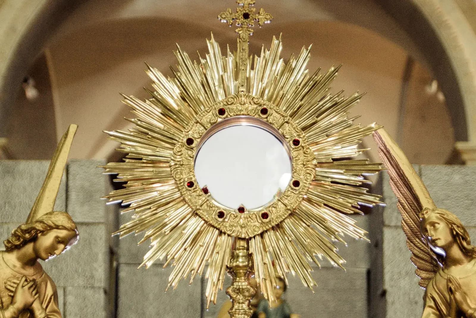 A golden monstrance holding the Blessed Sacrament, flanked by two adoring angels.