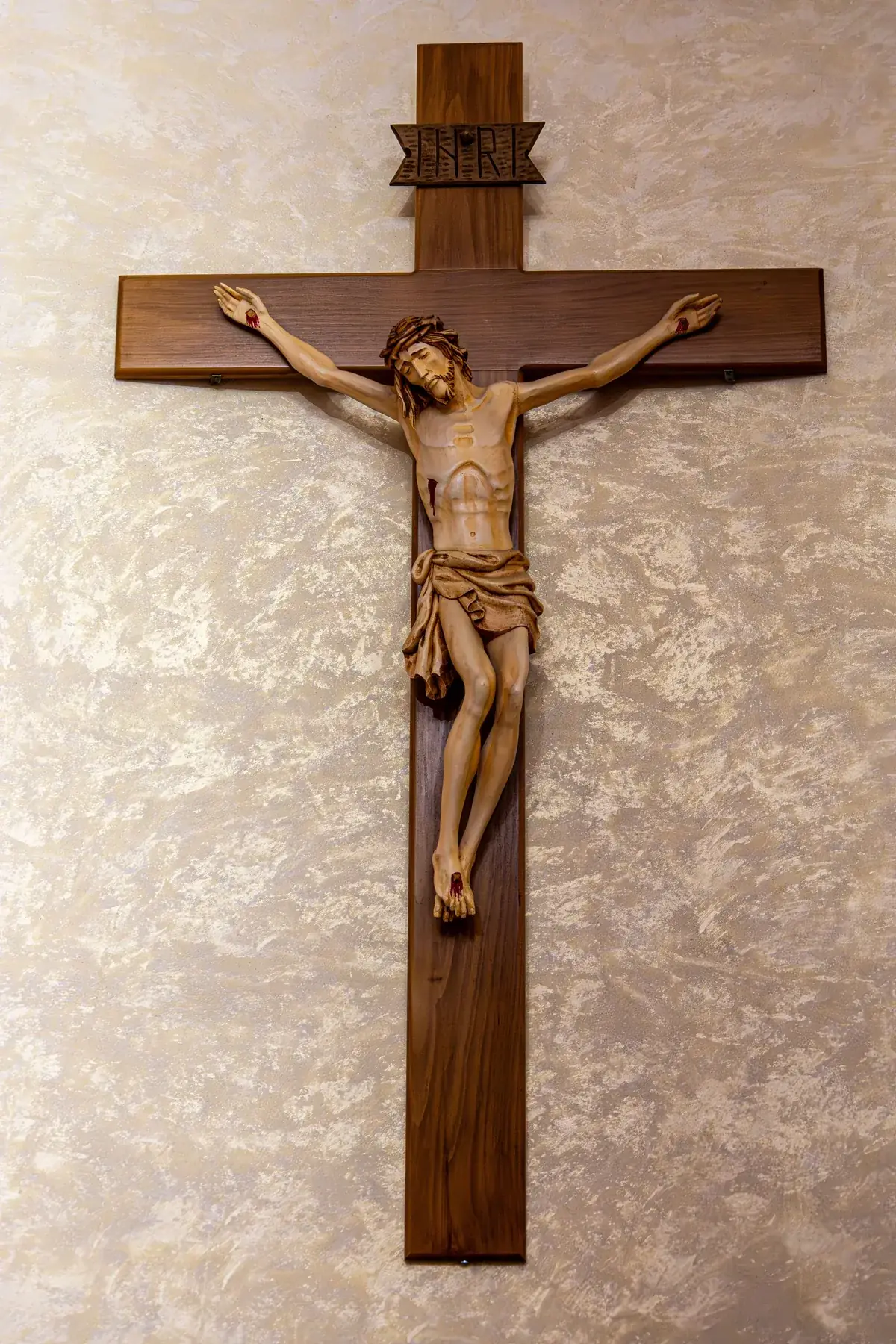 A carved wooden crucifix of Christ mounted on a softly lit wall.