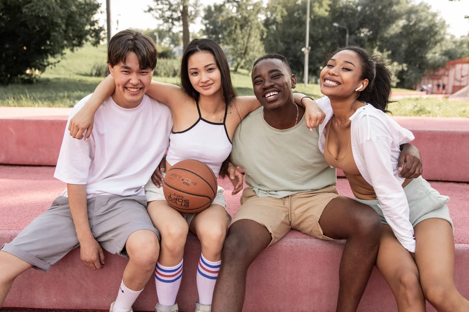 Four friends seated close together at golden hour, arms around one another’s shoulders, laughing.