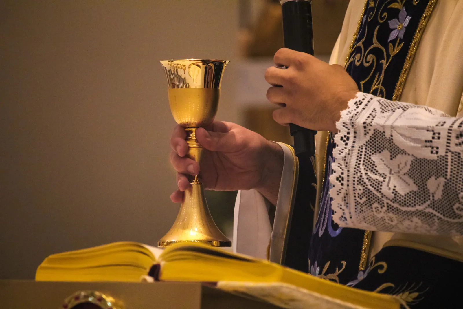 A priest elevating the chalice at the altar above an open Bible.