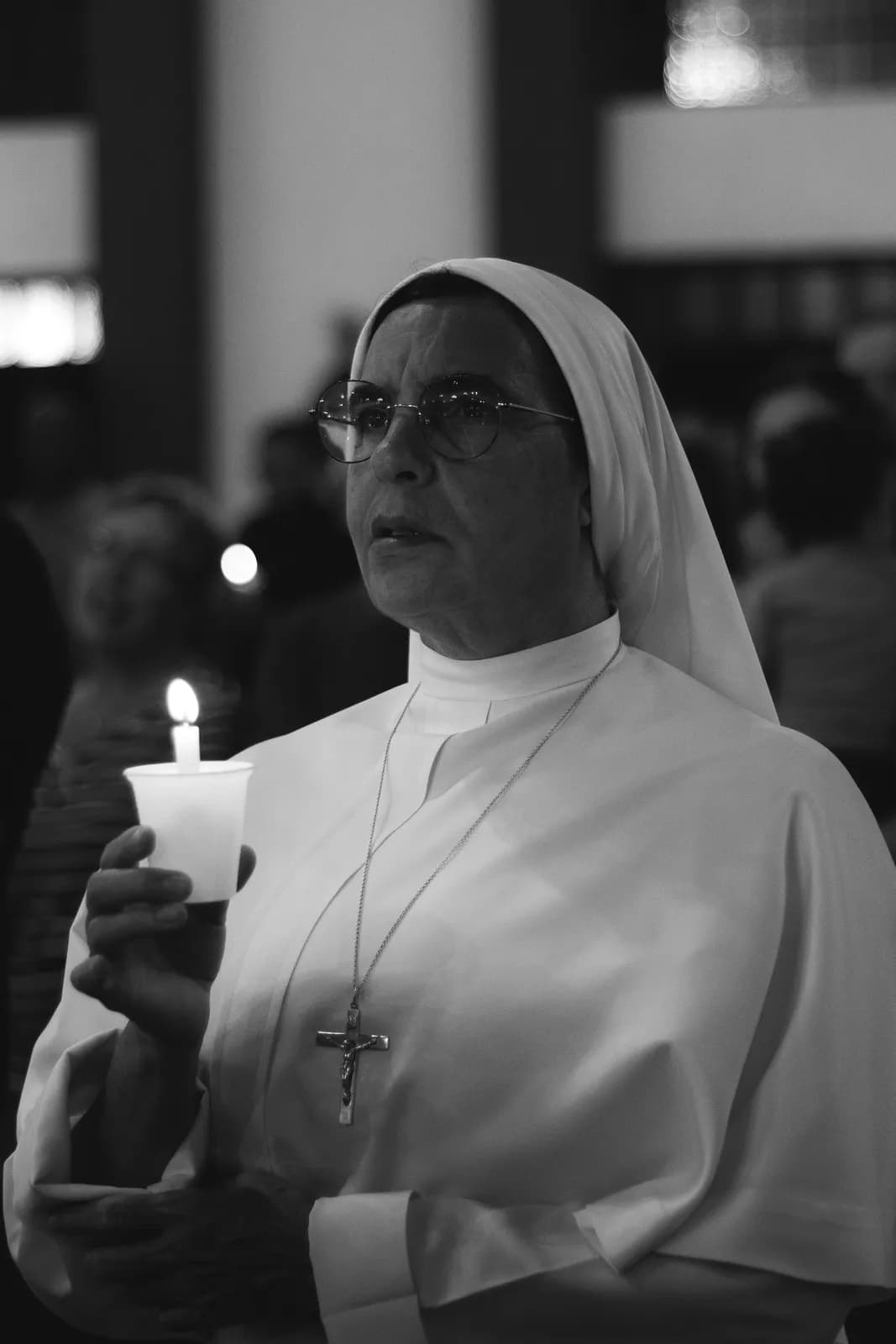 A religious sister holding a candle in prayer.