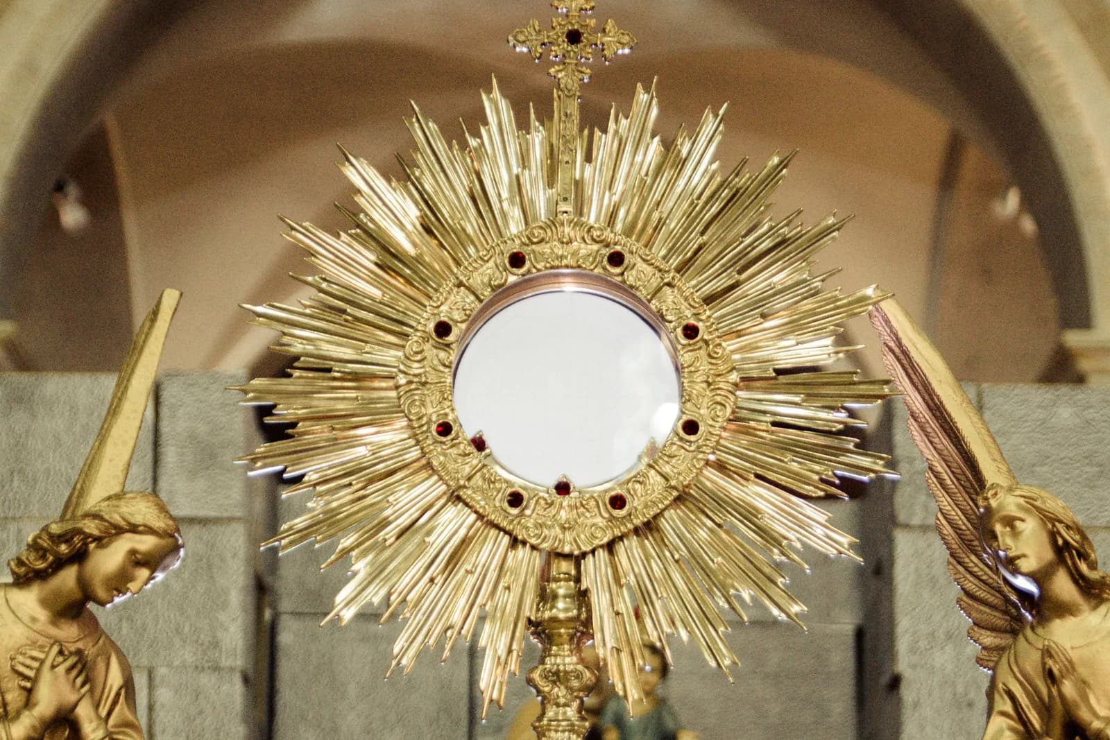 A golden monstrance holding the Blessed Sacrament, flanked by two adoring angels.