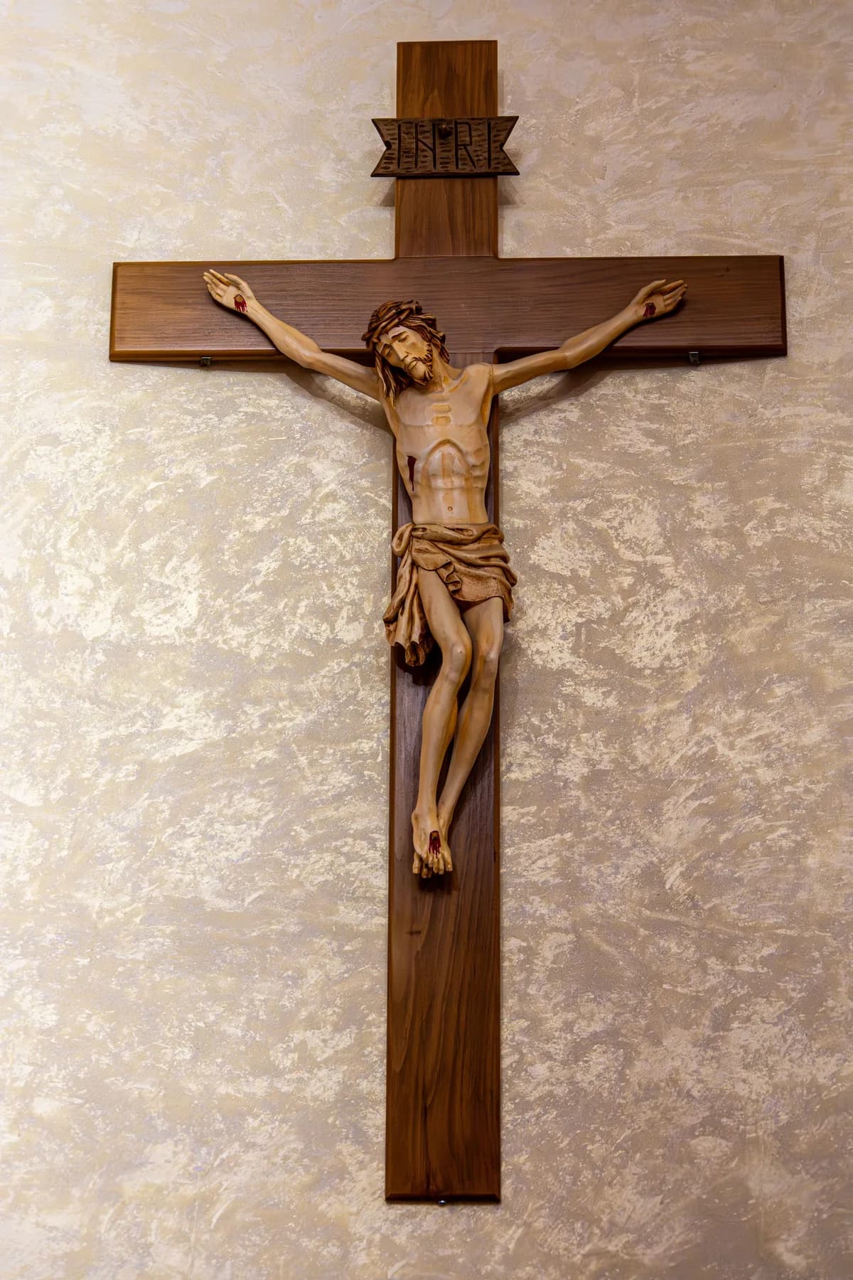 A carved wooden crucifix of Christ mounted on a softly lit wall.